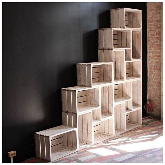 Wooden fruit crates stacked into a right hand triangle shape for bookshelves against a black wall.