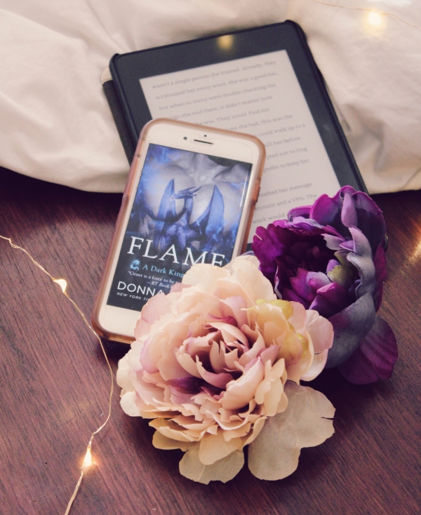 Iphone with picture of cover on top of kindle with text, two flowers in front of them, pink and purple