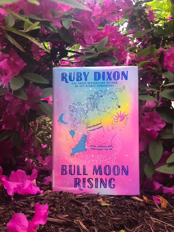 Hardbound edition of bull moon rising in front of a bush of bright pink flowers
