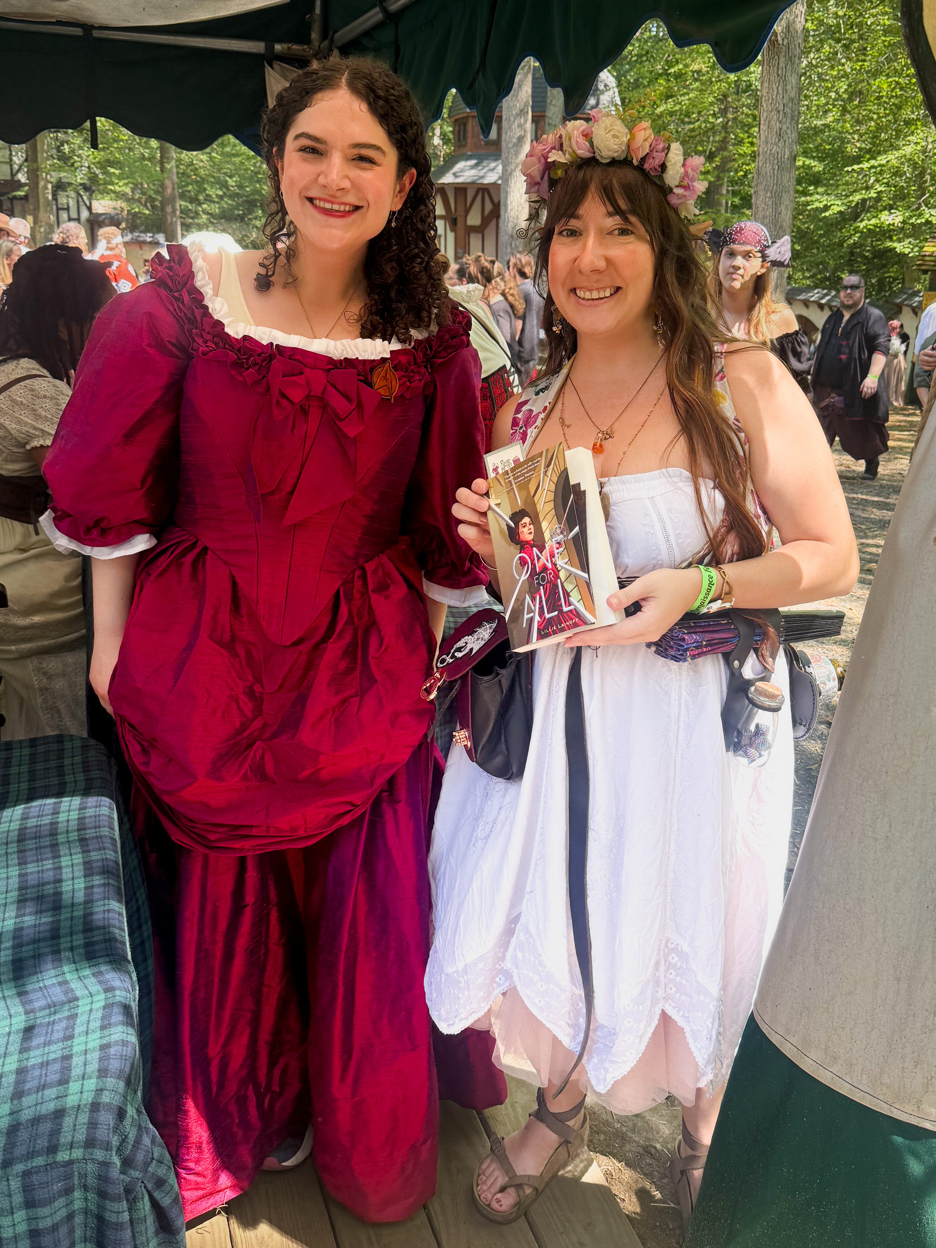 Kaite and Lilli Lainoff at the Maryland Renaissance Festival with Kaite holding Lilli's novel One for All. 